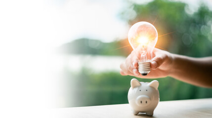 Creative saving of energy and money. A bright light bulb means innovation and a piggy bank is a...