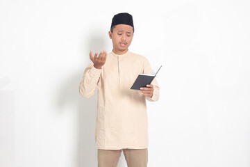 Portrait of confused Asian muslim man in koko shirt with peci difficulty understanding the contents...