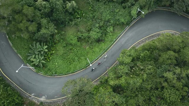 drone shot of young asian people riding bicycle on s-shaped rural road