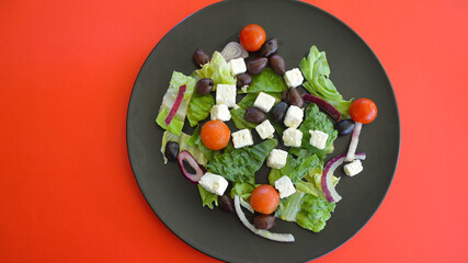 A Greek salad on a black plate against a colorful background.