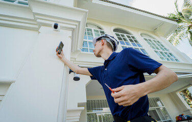 A technician installs a CCTV camera on the facade of a residential building.