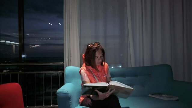 Woman reading a book siiting on sofa at night. 4k footage UHD 3840x2160 