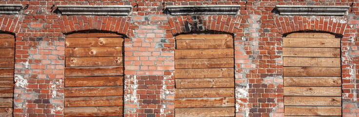 The windows of the brick building are boarded up. The windows in the building are tightly closed with old boards. Red brick building with blocked windows.