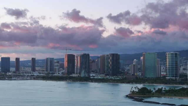 Pastel lilac pink purple clouds above Kaka Ako district in modern Honolulu downtown. Modern buildings of Ala Moana area at cinematic sunset. Scenic Ala Moana beach on Magic island, Oahu Hawaii 4K USA