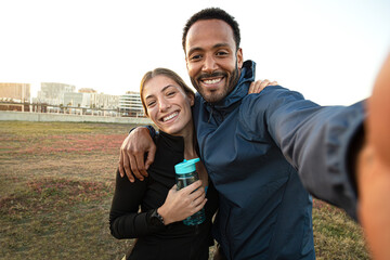 Multiracial couple taking selfie after workout outdoors. Sporty couple taking self portrait after running in the park.