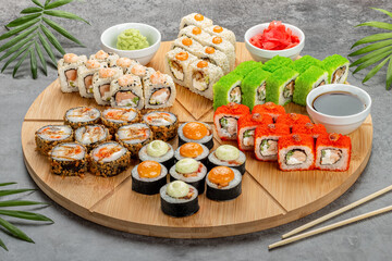 Assorted sushi rolls served on a wooden round board. Top view of seafood, various maki rolls, sashimi and nigiri with caviar, shrimp, salmon, eel, soy sauce, wasbi and ginger.