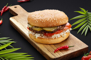Classic burger with beef, cucumbers, cheese, tomatoes, onions and vegetables on a wooden board with pepper.Dark background. Food photos. Advertising for the menu.