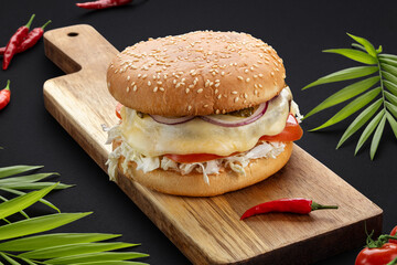 Delicious juicy burger with melting cheese, tomatoes, onions and vegetables on a wooden board.Dark background. Food photos.