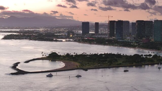 Scenic Ala Moana beach on Magic island, Oahu Hawaii 4K USA. Pastel rose gold clouds above Kaka Ako district in modern Honolulu downtown. Modern buildings of Ala Moana area at cinematic sunset