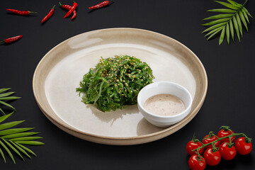 Seaweed chuka salad with sesame seeds in a bowl with nut sauce. Black background with tomatoes and peppers. View from above