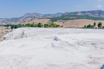 White travertine terraces dominate the landscape with hills under a clear blue sky, in Turkiye