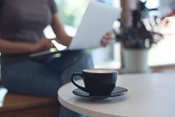 Woman working on laptop computer in coffee shop, business casual, freelance at work, people lifestyle. Black coffee cup on table, freelancer working on laptop as background