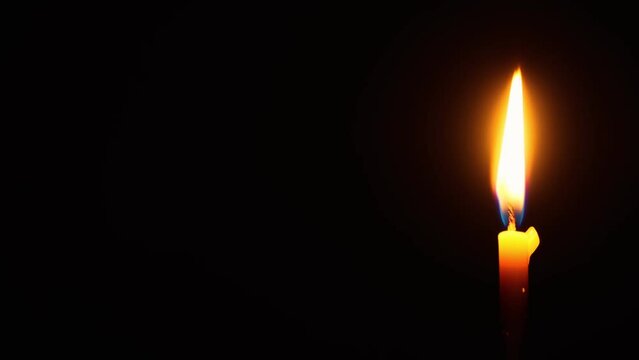 A funeral candle burning in total darkness. The concept of religion, mourning and memory. Close-up of a burning candle.