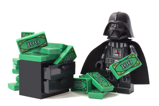 Lego minifigure of Darth Vader  or Star Wars male is counting his money green banknotes isolated on white. Editorial illustrative image of finance and banking.