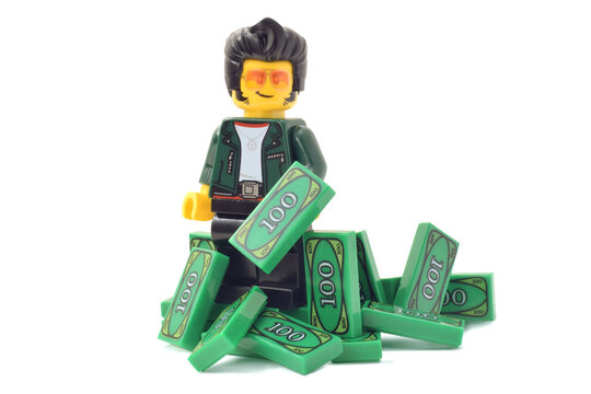 Lego minifigure of happy male is counting his money green banknotes isolated on white. Editorial illustrative image of finance and banking.