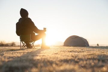 キャンプ場でコーヒーを飲みながら朝日を眺める男性
