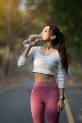 Young woman takes a break and drinks a water bottle after exercising in the park.