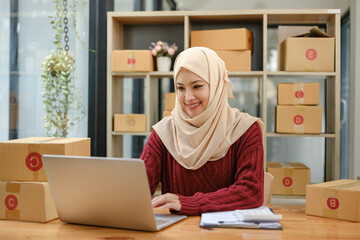 A portrait of a successful young Asian Muslim female online seller sits at her working desk with a...