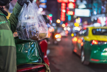 A delivery rider carrying a large food order in a plastic bag on a busy city street at night..