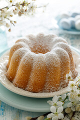 Bundt cake, Babka sprinkled with powdered sugar on a festive table decorated with spring flowers, close up view. Easter pastry