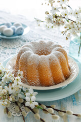 Bundt cake, Babka sprinkled with powdered sugar on a festive table decorated with spring flowers, close up view. Easter pastry - 745002954