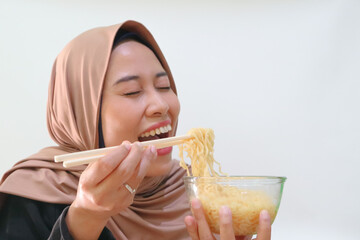Portrait of happy smiling Asian hijab woman using chopsticks eating instant noodle, noodles soup in...