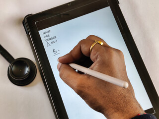 Picture of a doctor writing a prescription on a tablet with stylus. Picture is depicting...
