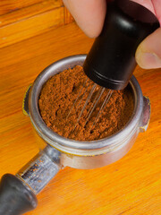 Fingers gripping a barista’s needle distribution tool in a portafilter basket, stirring the bed...