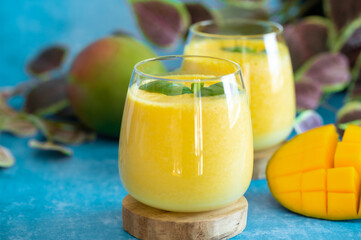 Fresh mango lassi in glasses on blue background with copy space.