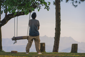 landscape and travel concept with solo freelancer man use tablet work at wooden swing under large...