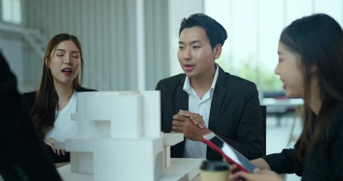 Asian businessman talking with team in meeting room. They dissing about building model and design together.
