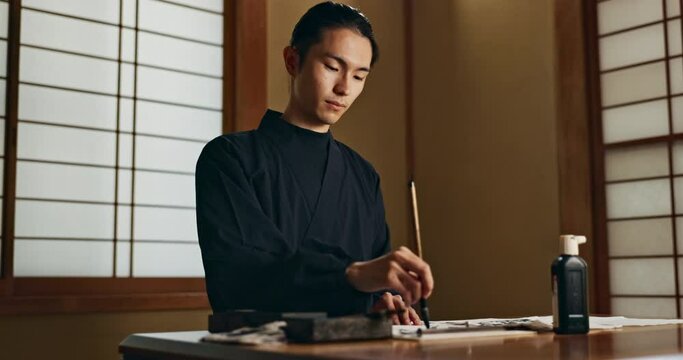 Japanese, man and writing with brush, traditional or ancient tools for art, black ink and inkstone on table. Script, font and alphabet with creativity and vintage pen for calligraphy and painting