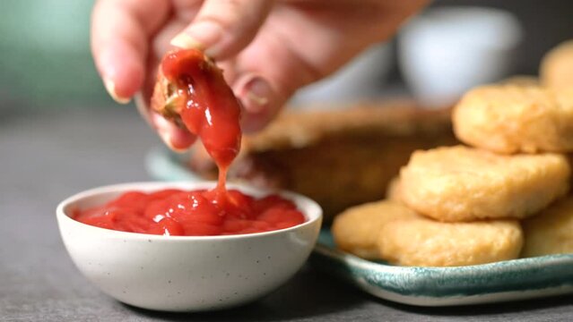 Crispy fried chicken wings, chicken nuggets and beef kebab in a plate. Kebab is Dipped into a Ketchup Bowl on a Table with Black Background a Macro Shot in 4K.