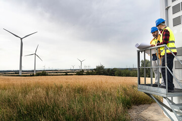 Two electrical technicians workers inspecting Wind turbine Electricity Power Station, using...