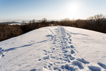 Fototapeta na wymiar Footprints on snowcovered hill slope, under freezing sky