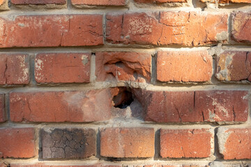 Close-up view of old molded red brick wall covered with craters from military shells, bullets,...