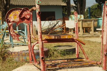 A red rocking horse made of steel is made in the shape of a red elephant in an outdoor playground in Thailand.