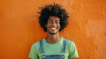 A young man with a joyful smile wearing a vibrant green t-shirt and denim overalls stands against...