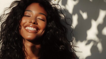 A woman with long wavy hair smiling with eyes closed basking in the warmth of sunlight filtering through leaves.