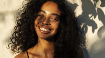 Smiling woman with closed eyes enjoying the sun her hair is curly and she is wearing a black top.