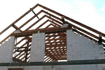 An "A" frame timber roof truss in a house under construction seen from the bottom, walls made of aac blocks, a rough window opening, a reinforced brick lintel, a scaffolding