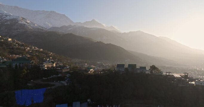 Early morning aerial view of Dharamshala city during sunrise, pan shot from city to snow-covered mountains, misty glow, 4k video
