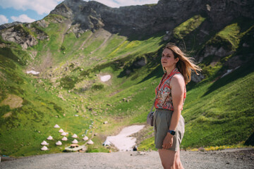 Naklejka premium A woman the background of mountains covered with vegetation. Hiking high in the mountains in summer, there is snow