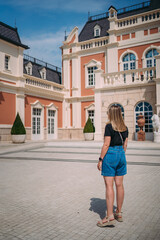 A girl with blonde hair in denim shorts and a black T-shirt against the background of a beautiful old castle. View from the back