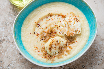 Turquoise bowl with cream-soup made of roasted cauliflower cabbage, middle closeup on a beige granite surface, horizontal shot