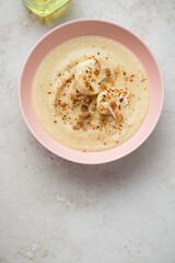 Bowl with roasted cauliflower cream-soup on a light-beige stone background, vertical shot with space, flat lay
