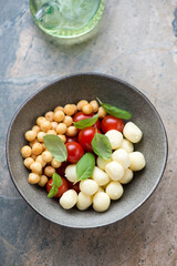 Bowl with scamorza cheese, smoked perlini balls, cherries and green basil, vertical shot on a beige granite background, elevated view