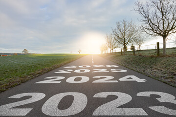 New year 2024 or straight forward concept. Text year 2023, 2024, 2025, 2026 written on the road in the middle of asphalt road with at sunset. Concept of planning, goal, challenge, new year resolution.