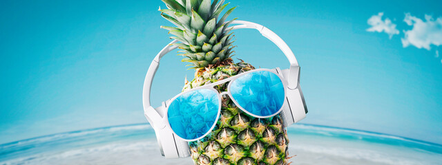 Funny pineapple with headphones at the beach