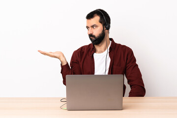 Telemarketer caucasian man working with a headset and with laptop holding copyspace with doubts.